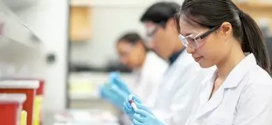 A group of scientists in a sterile laboratory environment, wearing white lab coats and blue gloves, conducting experiments with petri dishes and test tubes on a workbench.