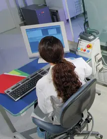 Overhead back view of ATCC scientist sitting at computer station near machinery in lab.