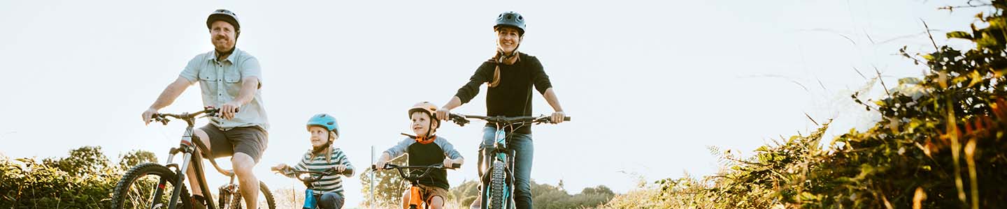 A smiling man and woman ride bikes with two young children on a clear, blue-sky day.