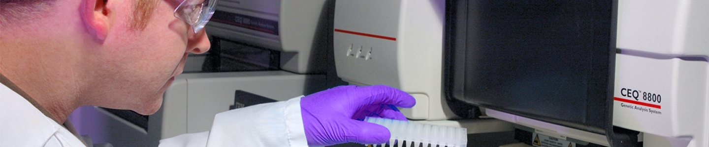 Profile view of scientist wearing lab coat, safety glasses, and gloves, putting well plate into CEQ 8800 Genetic Analysis System.