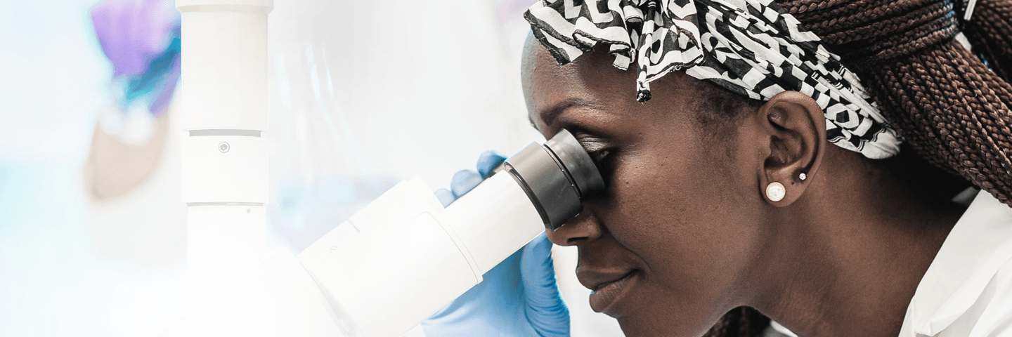 Female scientist wearing lab coat and gloves looking into a microscope.