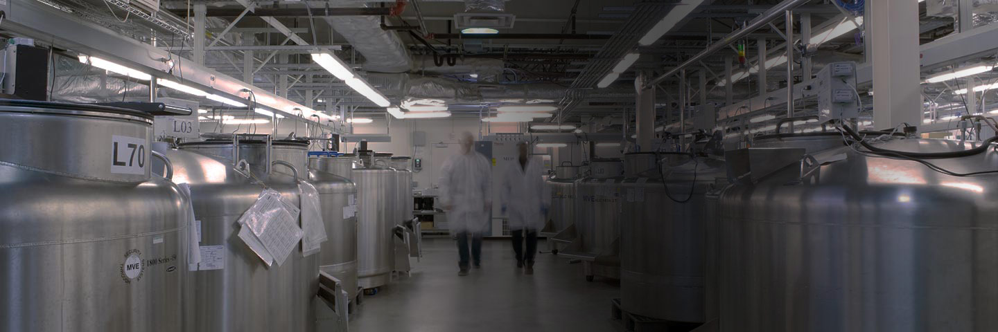 Two scientists walking between rows of cryo-tanks in a biorepository.