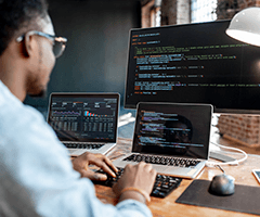 Black man sitting at a desk facing three computer screens, typing on a keyboard.