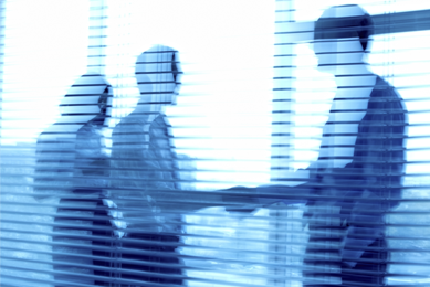 Two businessmen shaking hands and a woman standing next to them behind a blurry window with shades.