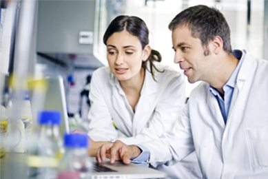 Female and male scientist in lab coats looking at laptop in a lab.