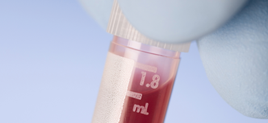 Close-up of gloved fingers holding closed plastic vial of red liquid.