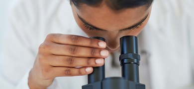 Scientist looking into a microscope, hand on one of the eye pieces.