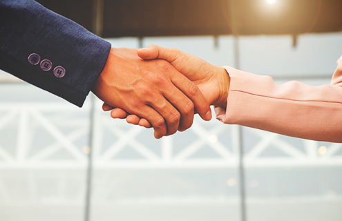 A man's hand and a woman's hands shaking. Both in business jackets.