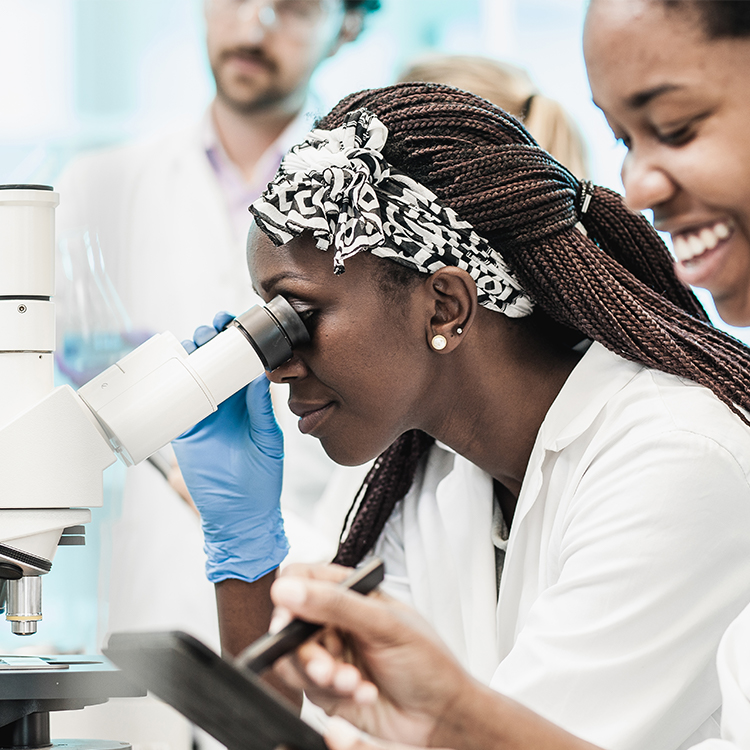 Female scientist wearing lab coat and gloves looking into a microscope.