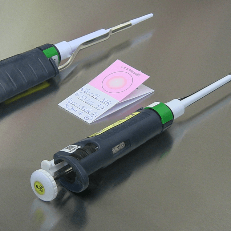 Two pipettes on either side of pink and white FTA Micro Card.