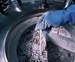 Gloved hand covered in ice, holding frozen vial, above cryopreservation tank filled with boxes of frozen vials.