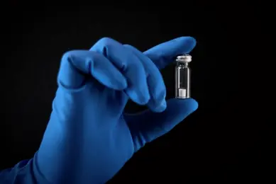 Blue gloved hand holding a Microquant vial between forefinger and thumb on a black background