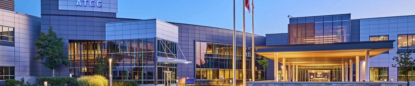 Exterior of ATCC office building in early evening with building lights on, flags on flagpoles.