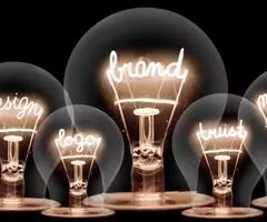 Photo of light bulbs with shining fibres in shape of BRAND concept related words isolated on black background