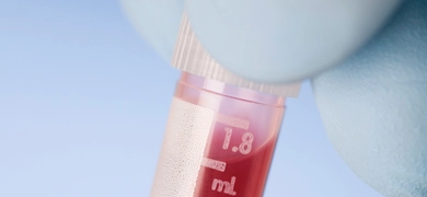 Close-up of gloved fingers holding closed plastic vial of red liquid.