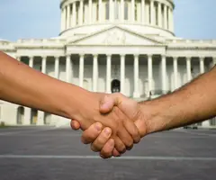 Closeup of two hands shaking with the US Capitol building in the background.