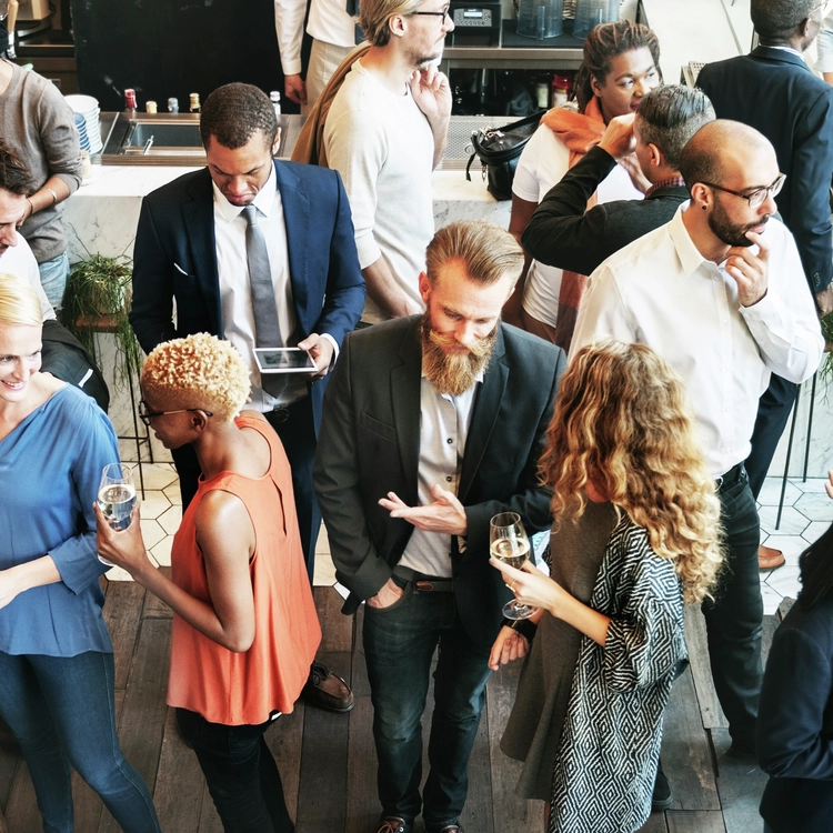 A group of professionals networking at a business happy hour, engaged in conversations while holding drinks in a modern venue.