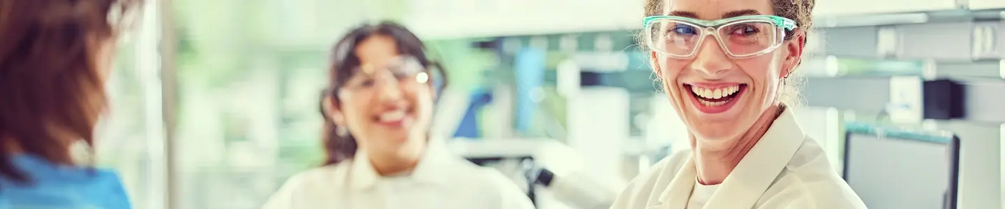 Three people in a lab, two in white coats and one in blue, with lab equipment in the background.