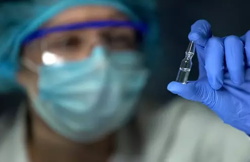 Gloved hand holding a small glass vial in a medical or laboratory setting.