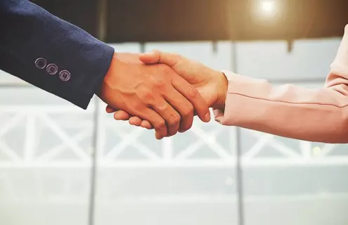 A man's hand and a woman's hands shaking. Both in business jackets.