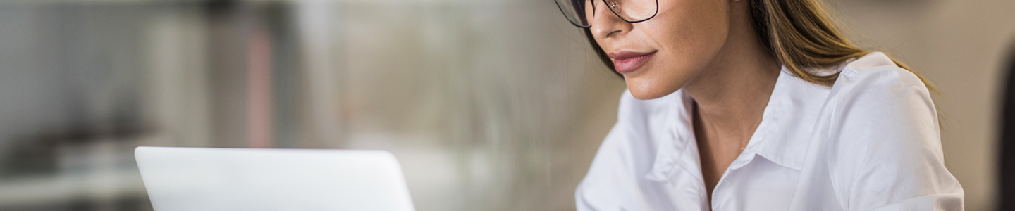 A woman wearing glasses looking at a silver, laptop computer.