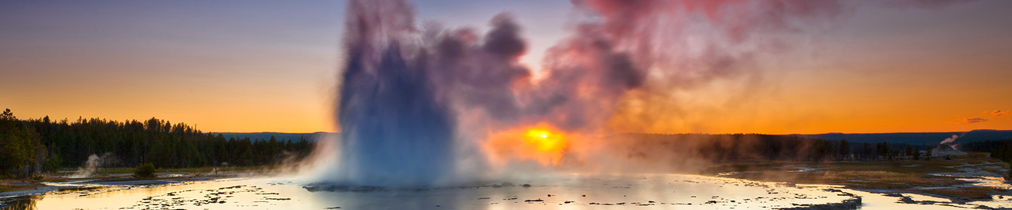 A plume of smoke rising from layers of slate-like liquid at Great Fountain Geyser in Yellowstone National Park at sunset.