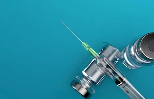 Syringe lying across a vial on its side on blue background