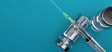 Syringe lying across a vial on its side on blue background