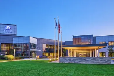 Exterior of ATCC office building in early evening with building lights on, flags on flagpoles.