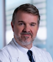 Portrait of Wesley Long wearing a white lab coat and dark tie, standing in a clinical setting with a blurred hospital background; a Houston Methodist logo is visible on the lab coat.