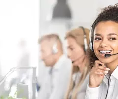 Young, black woman wearing a head set smiling with other people wearing head sets in the background.